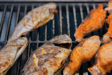 Process of cooking salmon steaks and mackerel fish on grill over charcoals at summer local food market - close up. Outdoor cooking, barbecue, gastronomy, seafood, cookery, street food concept