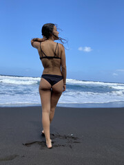 Young woman with black hair walking on the volcanic beach of Lanzarote