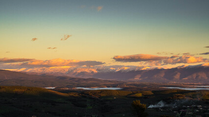 countryside landscape with snowy mountains and clouds at sunset