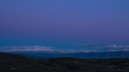 countryside landscape with snowy mountains and clouds at sunset with purple hues reaching blue hour