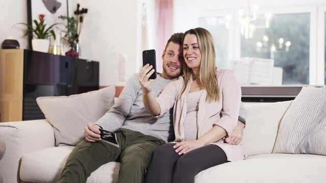Young pregnant happy couple sitting on couch telling friends family getting a baby via live stream with ultra sonic picture shot in 4k
