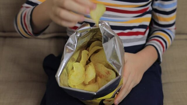 Little boy sitting on sofa, eating chips from packet