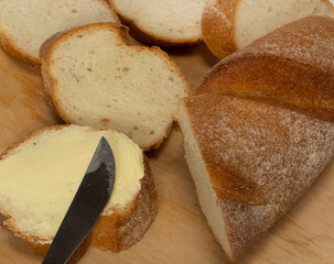 Fresh baguettes with crispy crust with butter chopped on a cutting board on a white table. Tasty breakfast. kitchen knife. High quality photo
