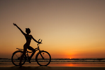 healthy alone woman ride on bicycle on empty sunset Goa India beach