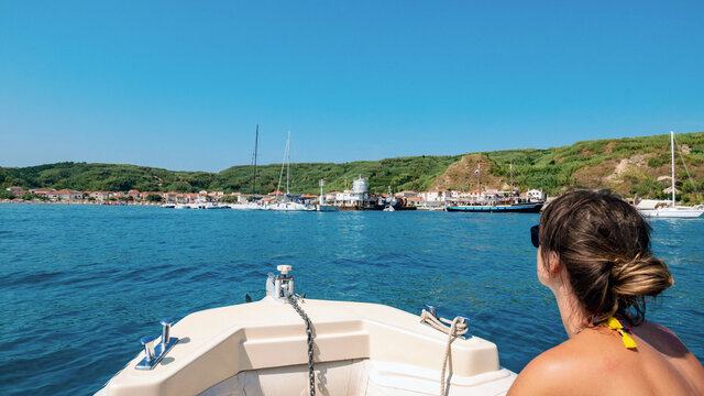 Young female on boat looking at idyllic small town on green island.