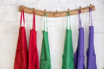 Brightly coloured cooking aprons hanging on wooden pegs.