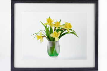 Home interior floral decor. Frame decorated flowers in vase on white table. Poster with narcissus on color background.