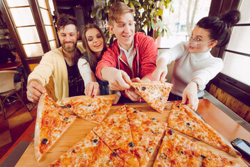 The company of guys in the pizzeria. Four friends in a cafe on the background of a large pizza on a...