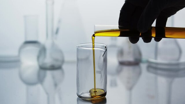 Pouring essential oil from a test tube into a flask in the laboratory. Glass flasks in the laboratory under backlit. Study of the beneficial properties of essential oils. Natural cosmetics production.