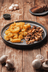 Fried potatoes with mushrooms on a gray plate next to fresh mushrooms