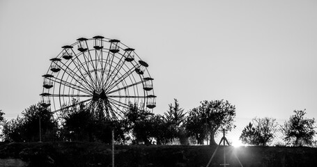 View of the silhouette of a Ferris wheel behind the trees at sunset