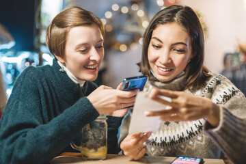 Friends split the bill using the app on their smartphone after a delicious dinner in a cafe.