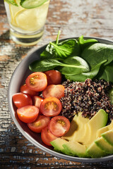 Dish of sliced tomato, avocado, basil and quinoa on rustic table