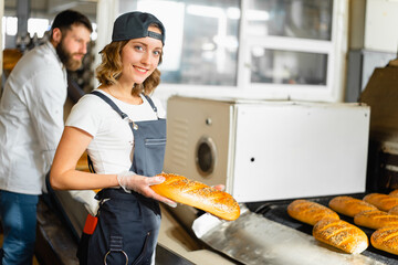 Portrait of a baker girl with bread in hands against the background of an automated line in a...