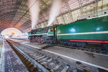 Obraz premium Retro steam train stands by the passenger platform.