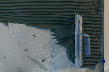 Close up of the hands of a master builder's man with a notched trowel, putting a tile adhesive...