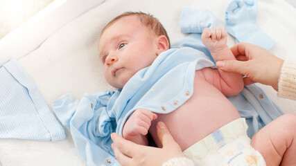 Closeup shot of caring mother undressing her little 1 months old baby boy lying on changing table....