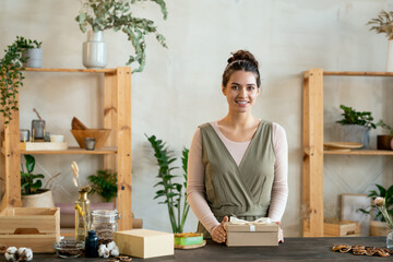 Young cheerful female in smart casualwear holding cardboard giftbox with present