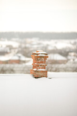 Old red brick chimney with white snow on roof