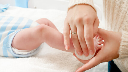 Closeup of mother cleaning newborn baby body and applying moisturizing baby oil with cotton pad