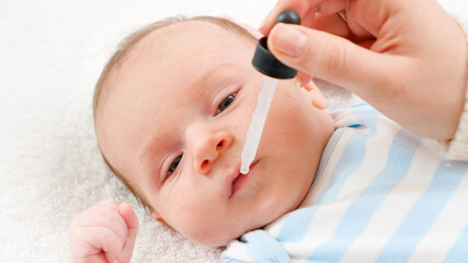 Closeup of giving vaccine from eyedropper or syringe to newborn baby boy