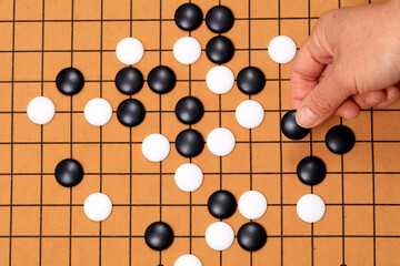 the game of go, chinese game go,  Close up view of hand playing black and white stone pieces on Chinese go game board.