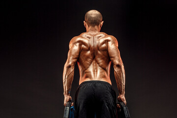 Fototapeta na wymiar Muscled shirtless male model showing his back muscles on dark background isolate.