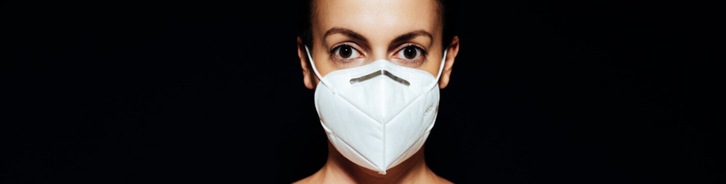 Portrait Of A Young Woman Wearing A KN95 Face Mask Against A Black Background