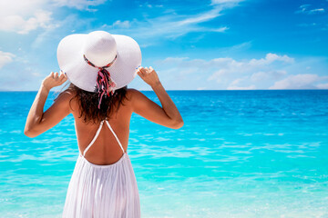 Summer holiday travel concept with a woman in white dress and hat looking at turquoise colored sea with copy space