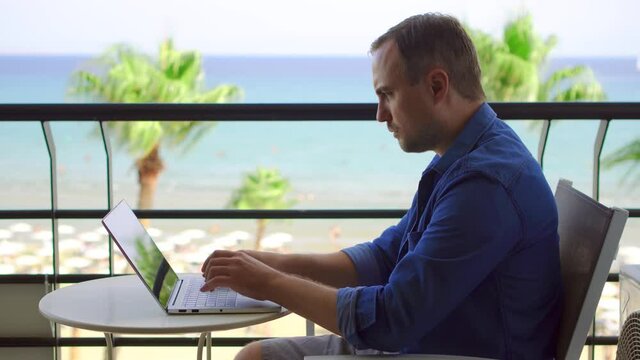 Businessman sit on balcony work on laptop at tropical beach resort. Young professional male freelancer typing on computer from remote home office. Concept of social distancing and lockdown