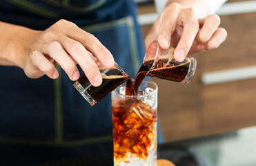 Barista making Ice coffee in a tall glass by pouring brew coffee  over ice on a old rustic wooden...