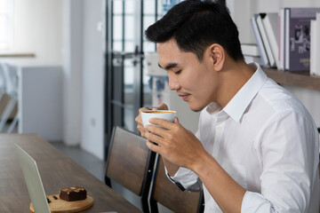 Young man smelling aroma of coffee in the cafe before drinking. Man drinking coffee with coffee cup in morning time.