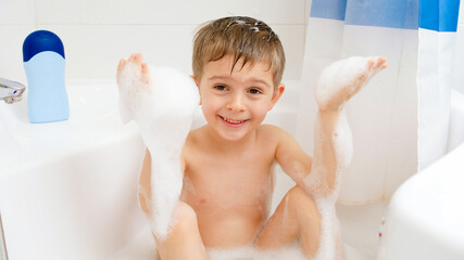 Funny little boy enjoying taking bath with foam at home