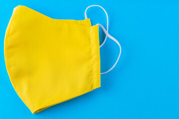 Reusable face mask made from yellow cotton. Face protective mask. Yellow protective mask on a blue background. Copy space