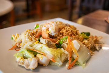 Stir fried noodles with shrimps, pork and vegetables on white dish. 