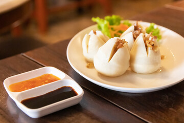 Boiled fish balls in white dish with sweet and spicy dipping sauce on wooden table.