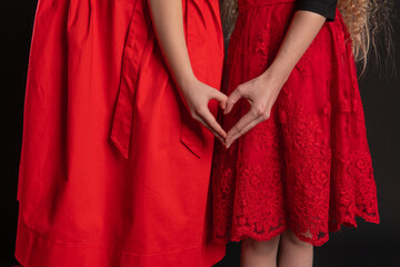 Fototapeta na wymiar Girl and baby sign of love hands keep the love Valentine's background, the design of valentine, on the floor hearts of romance. February 14 holiday. emotions forever, joy in red girl dress, barefoot