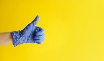 Closeup of doctor hand in blue glove with thumb up on yellow background. Good medical care banner....