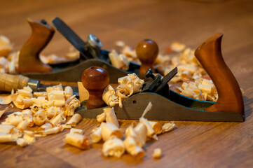 An old wooden jointer and a chisel with shavings lie on the wooden floor. Selective focus. 