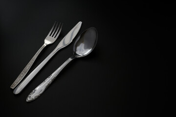 fork, spoon and knife on a dark background. Copy space