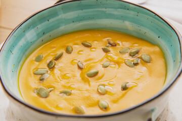 pumpkin soup with seeds in a beautiful plate on the background of the table and chopped pieces of pumpkin