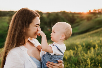 Young beautiful mother with her little daughter hug, kiss, laugh and walk in nature at sunset. Photo of a mother with a small child at sunset.