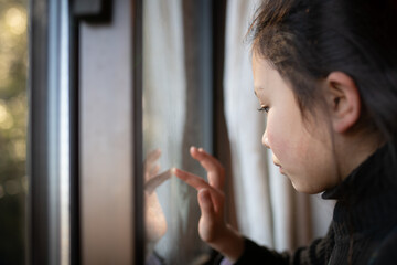 窓に指で落書きをする少女
