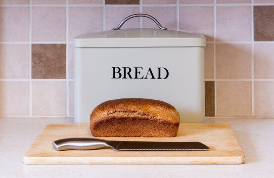 Loaf of home baked wholemeal bread on cutting board with knife in front of a bread tin
