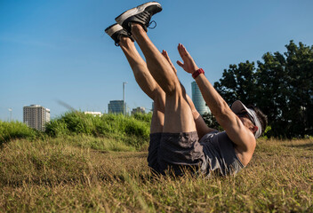 An athletic and fit asian guy does V-ups on the grass at an open field near the city. Abdominal...