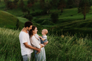 Young beautiful family with a little daughter hug, kiss and walk in nature. Photo of a family with a small child in nature.