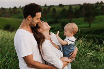 Young beautiful family with a little daughter hug, kiss and walk in nature. Photo of a family with a small child in nature.