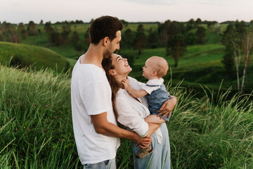 Young beautiful family with a little daughter hug, kiss and walk in nature. Photo of a family with a small child in nature.