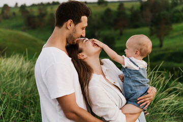 Young beautiful family with a little daughter hug, kiss and walk in nature. Photo of a family with a small child in nature.