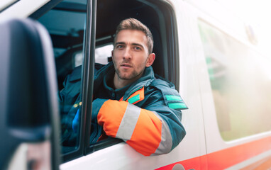 Professional and confident young man doctor looking on the camera with ambulance background